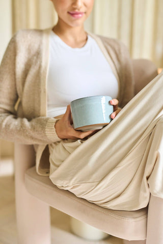 Woman holding a light blue mug with a beige blanket over her lap indoors - Pangolins