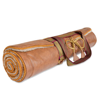 A rolled tan yoga mat with a cream sherpa lining, secured with a patterned strap and rope tie, shown on a white background.