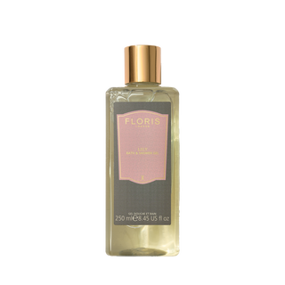 A rectangular glass bottle of FLORIS Lily Body & Skin Care, filled with pale yellow liquid and featuring a metallic gold cap and a dark gray label with a pink center panel.