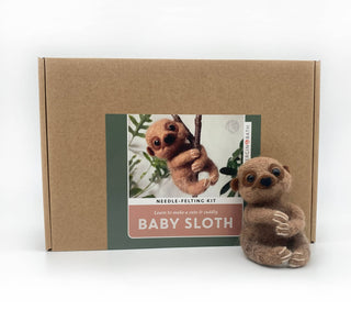 A needle felting kit box labeled 'BABY SLOTH' next to a small felted baby sloth toy on a clean white background.