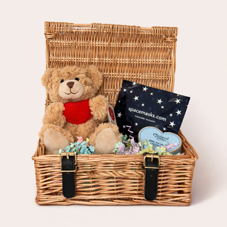 Wicker gift basket with teddy bear, space-themed items, and candy on a white background