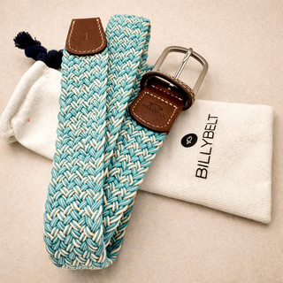 Teal and white woven belt with brown leather buckle on a beige surface, next to a white pouch with 'BILLYBELT' branding.