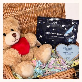 Teddy bear with a heart, spacemasks product, and dark sea salt caramel in a wicker basket.