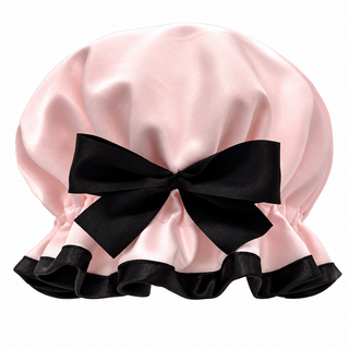 A Shower Goddess light pink satin shower cap with a large black satin bow at the front and a black satin ruffled trim along the bottom edge, shown against a plain white background.