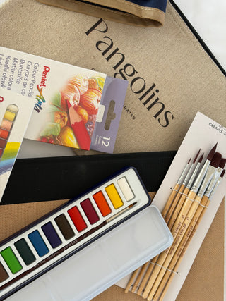 Art supplies including color pencils, watercolor set, and brushes on a table with 'Pangolins' branding.