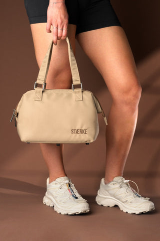 Person holding a beige handbag with 'Staerke’ branding on a brown background - Pangolins