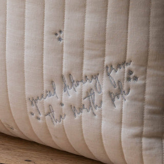A close-up of a cream-colored quilted Christmas sack with vertical channel stitching and embroidered gray text reading 'special delivery from the north pole' alongside small star details, resting on a wooden surface.