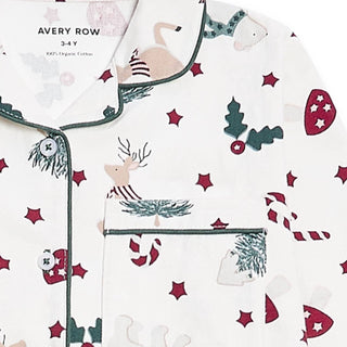 A close-up of a children's long pajama shirt by Avery Row, featuring a festive Christmas print on an off-white background. The print includes a reindeer, polar bear, candy cane, holly, pine branches, and red stars, with dark green piping and buttons.