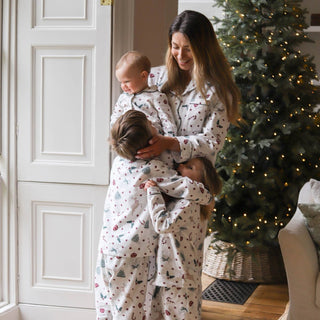 A family of four wearing matching holiday-themed pajamas, hugging in a cozy living room with a decorated Christmas tree in the background.