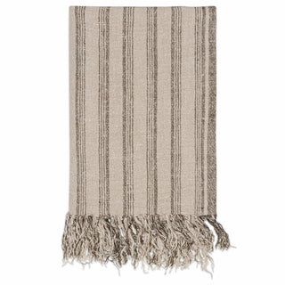 A Nkuku woven throw blanket with vertical stripes in beige and brown, finished with fringed tassels on one end, shown against a plain white background.