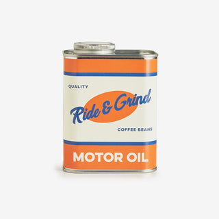 A rectangular metal can of Ride & Grind Motor Oil filled with coffee beans, featuring an orange, white, and blue label on a light gray background.