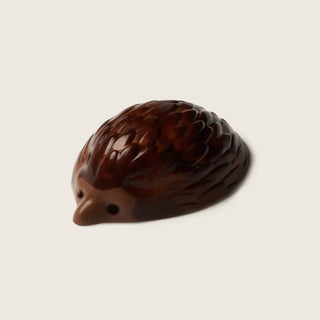 A small hedgehog figurine with dark brown textured spines and a lighter brown face, shown on a plain light beige background.